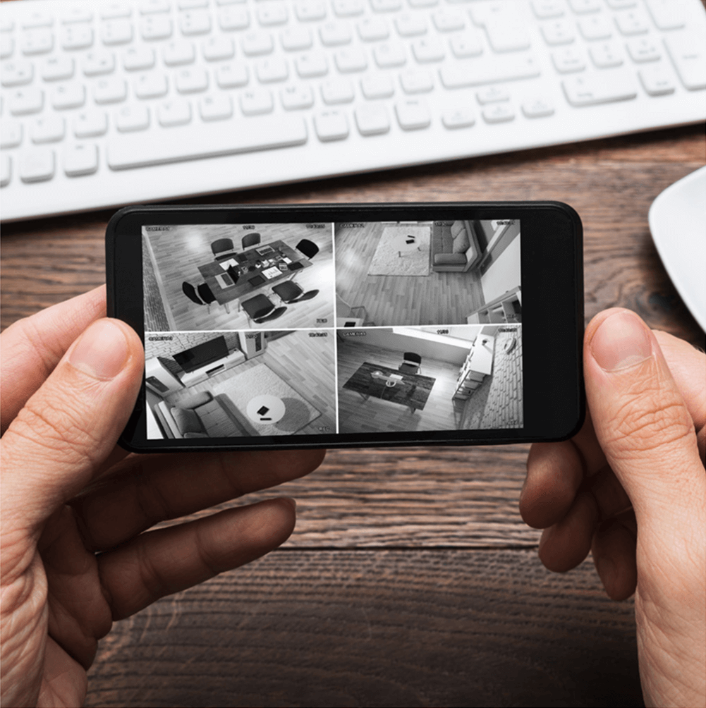A person holding a smartphone showing four live security camera views of a home interior.